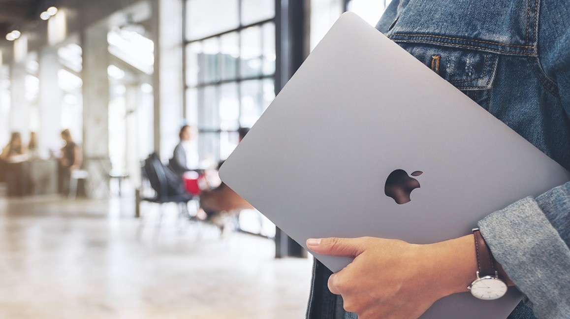 Das Bild zeigt ein zugeklapptes Apple MacBook, das getragen wird.